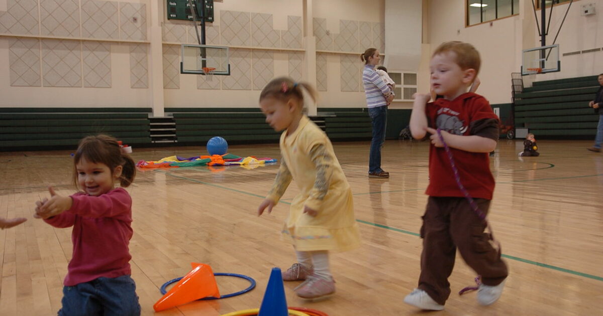 Niños realizando una actividad motriz guiada en un gimnasio escolar con conos y aros